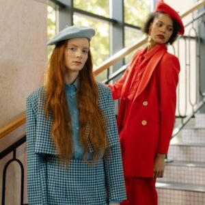 Home Two fashion models in colorful outfits posing stylishly indoors on a staircase.