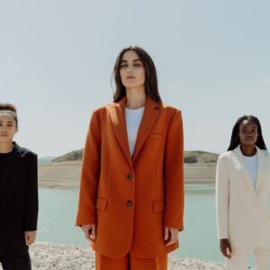 Home Three stylish women in suits posing confidently outdoors by a serene lake.